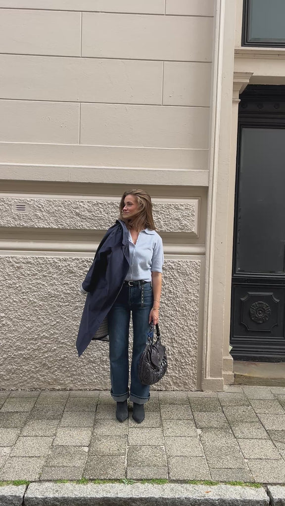 Palomah in Heather Blue in Bewegung, zur weißen Jeans mit dunkelblauem Mantel über dem Arm